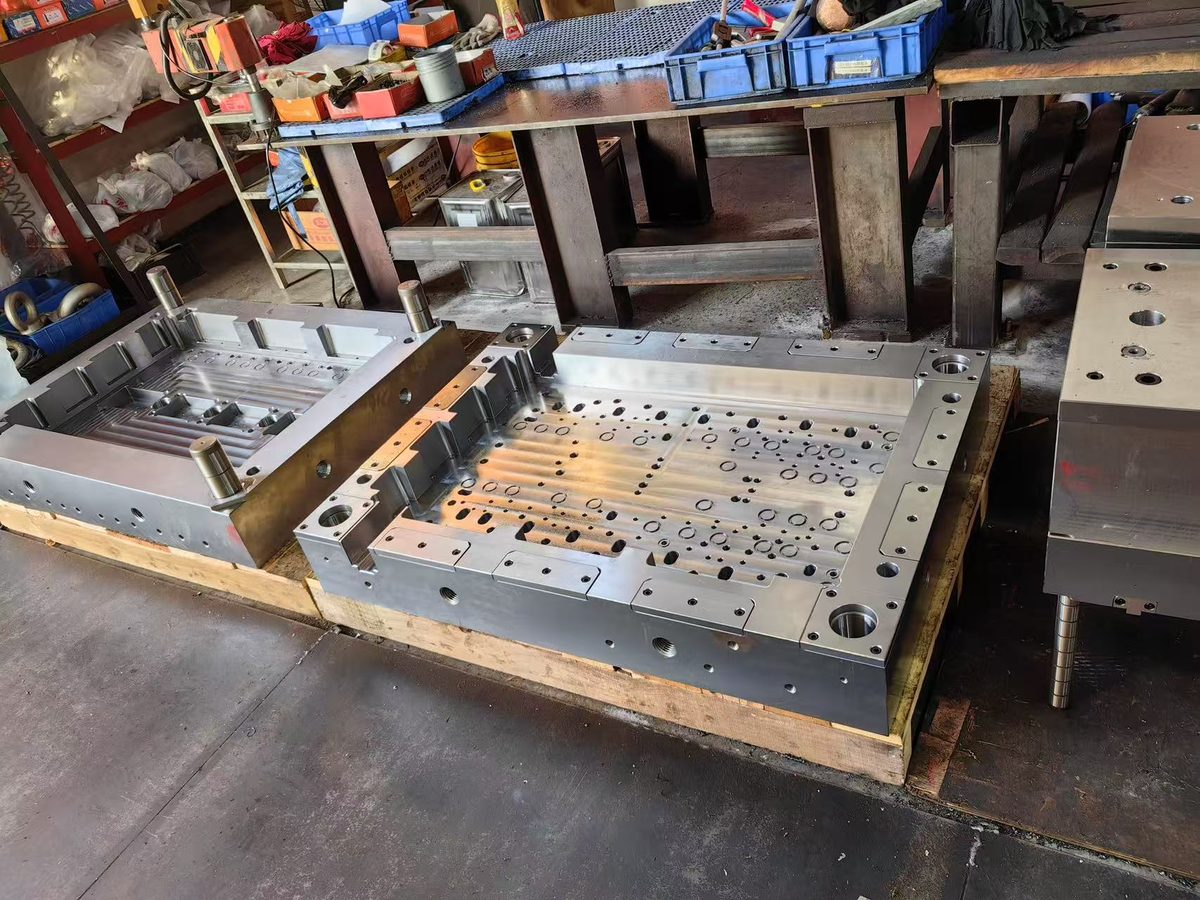 Two machined mold base plates on the workshop floor, cavity pockets, tapped holes and guide bores finished